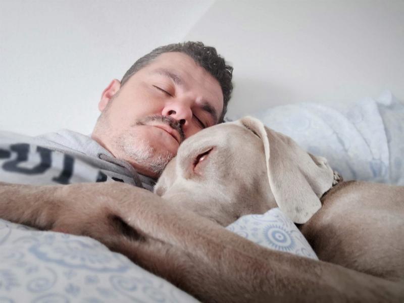 man and dog cuddling and sleeping in bed