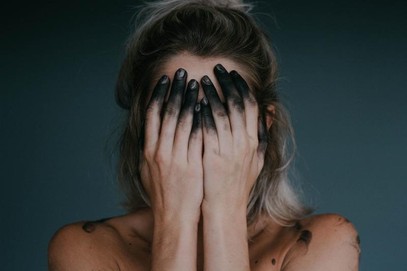woman with grey dipped fingertips covers her face with her hands