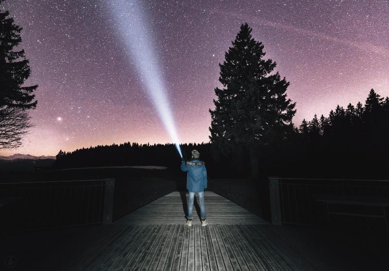 man points flashlight up to pink starry sky while standing on  bridge