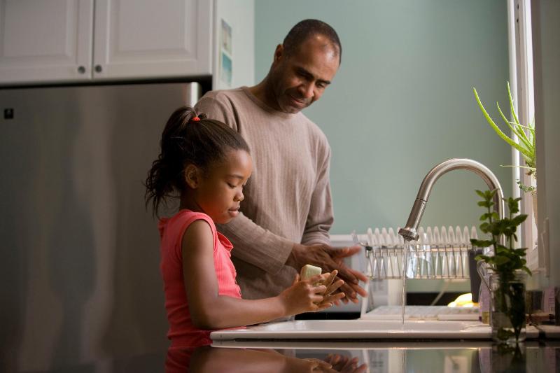 little girl doing dishes with her dad with water running