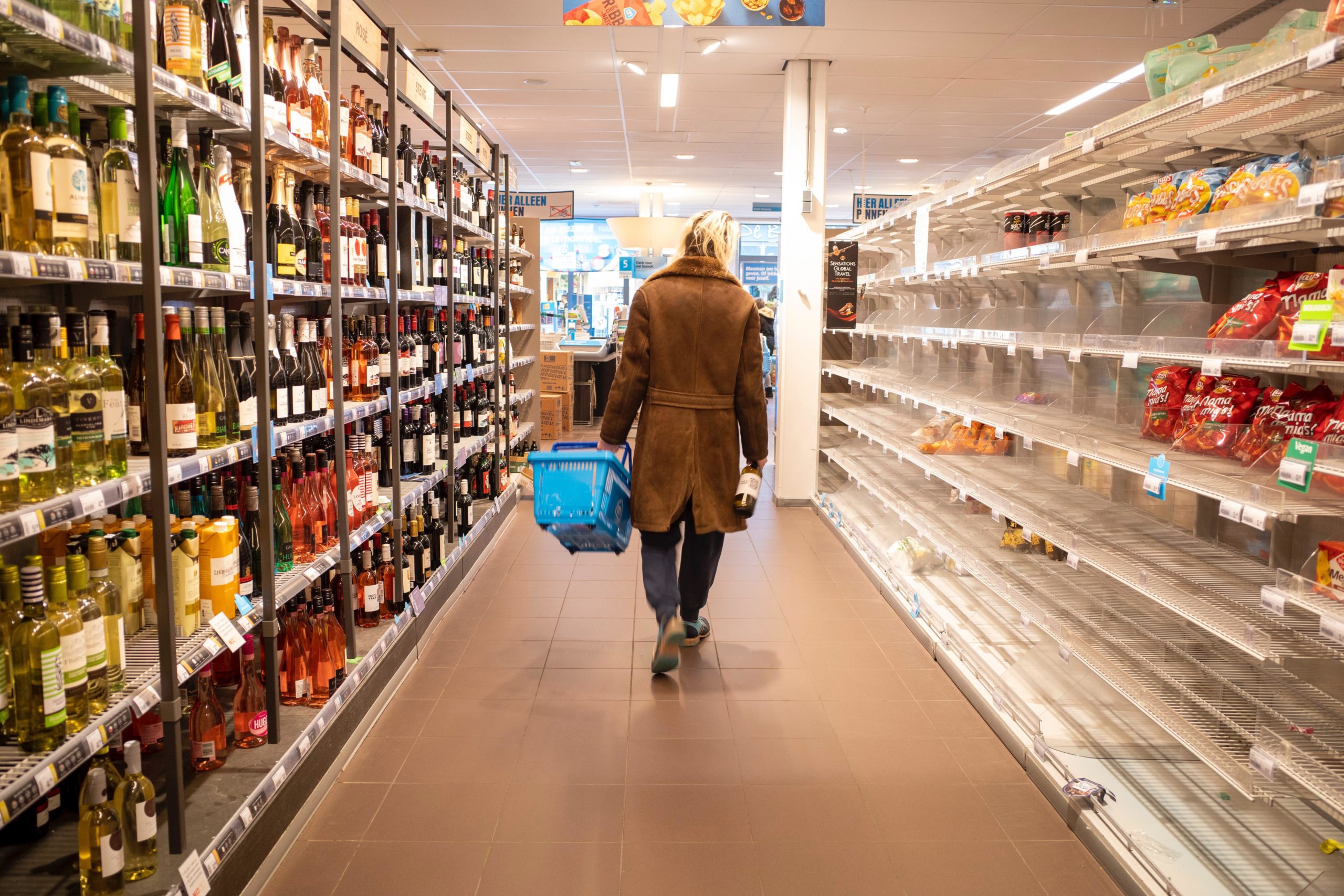 woman walks with basket in grocery store with empty aisle