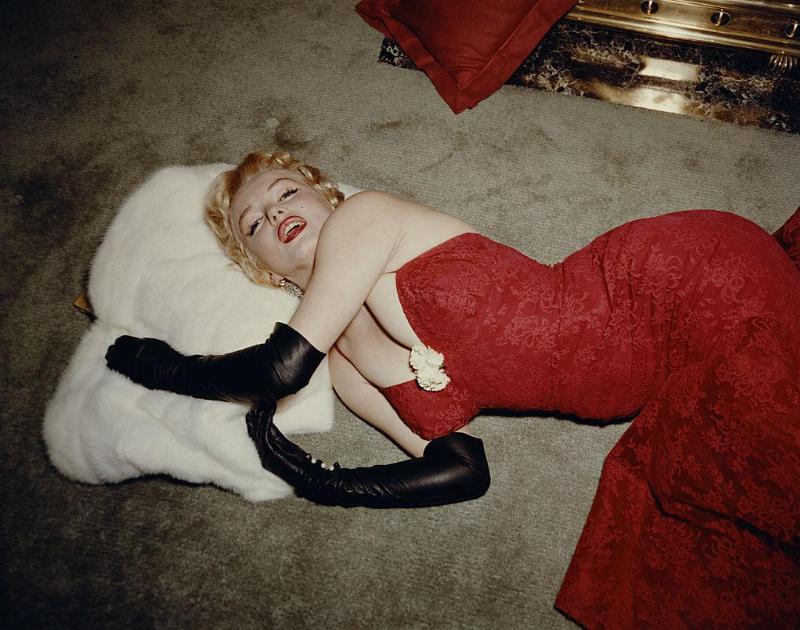 1955: EXCLUSIVE American actor Marilyn Monroe (1926 - 1962), wearing a red brocade evening gown and long black gloves, lying on a carpet and using a white fur stole as a pillow. (Photo by Gene Lester/Getty Images)