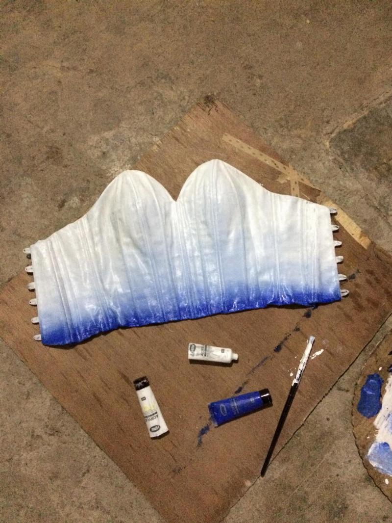 corset top of dress with fresh paint on it beside blue and white paint palette and brush