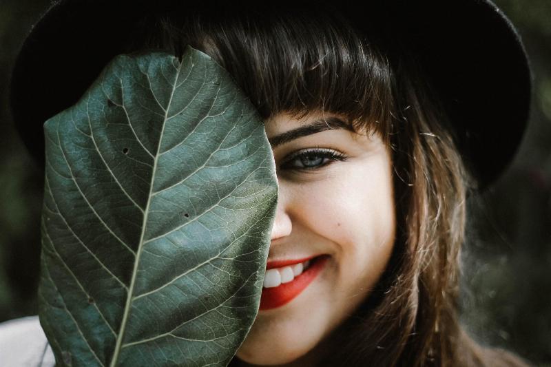 woman smiles while hiding half her face with a leaf