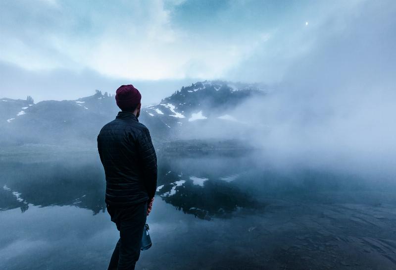 man sits in the mist of mountain reflection