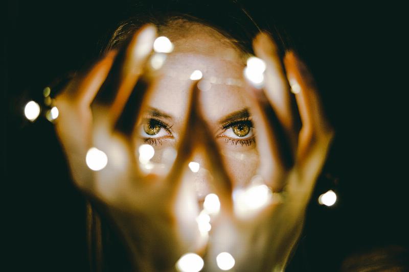 woman holds string lights by her face lighting up her eyes