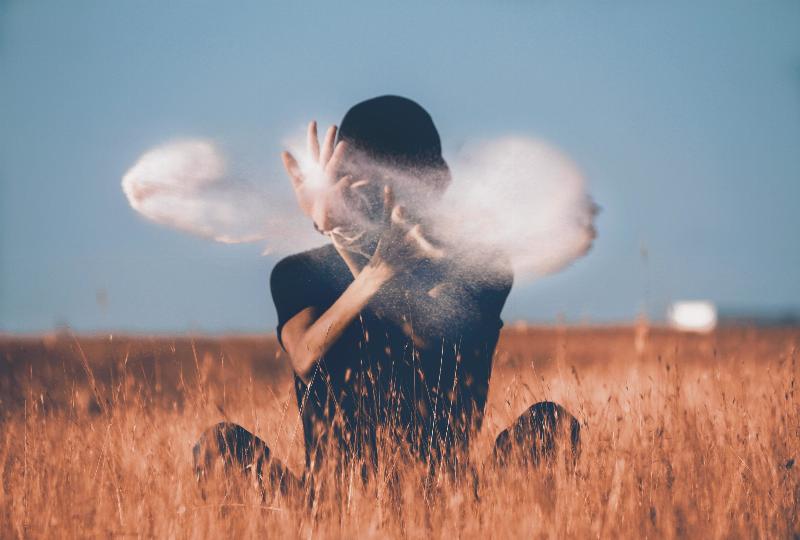 man sits in field and guides smoke around his face with his hands