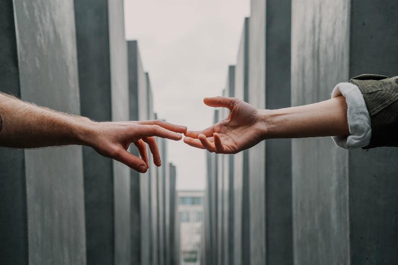 two hands reaching from each other from both sides of grey wall