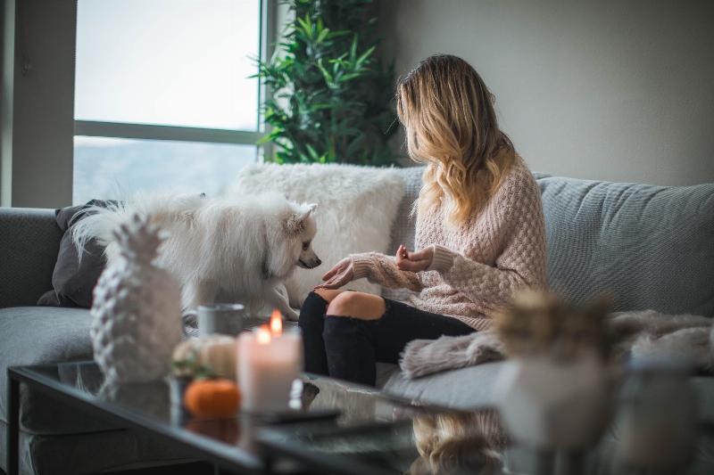 woman sits on couch with lit candle and her dog