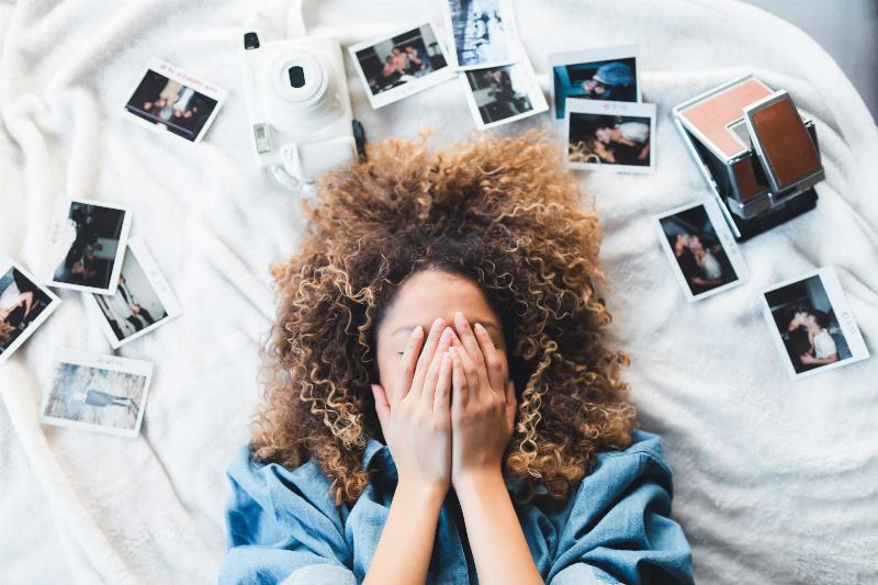 woman hiding her face with her hands in bed surrounded by printed pictures