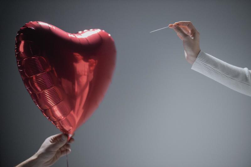 heart balloon about to pop by person holding needle