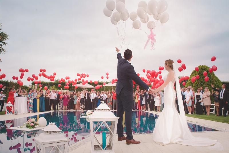 bride and groom and guests throw up red balloons
