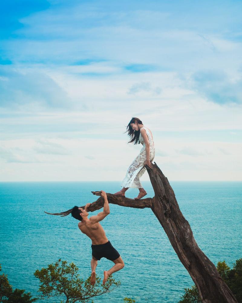 man climbc tree to reach woman by ocean