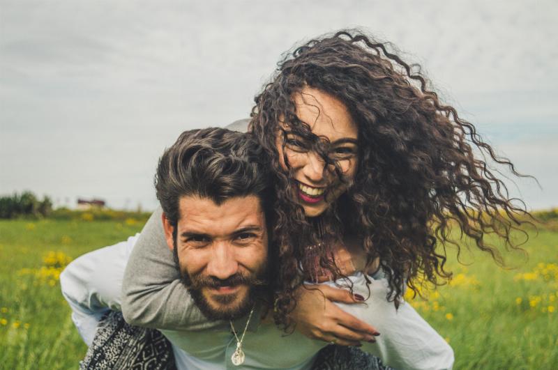 woman piggy backs on man's back and laughs in a field