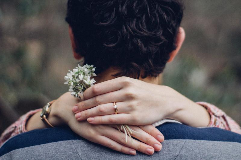 hand holding flower and wearing ring wrapping around man's neck