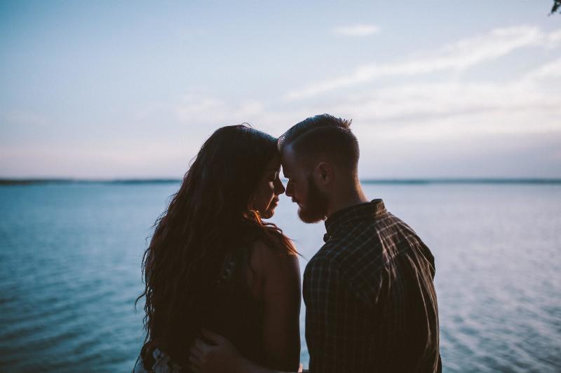 man and woman sit by the water and touch foreheads