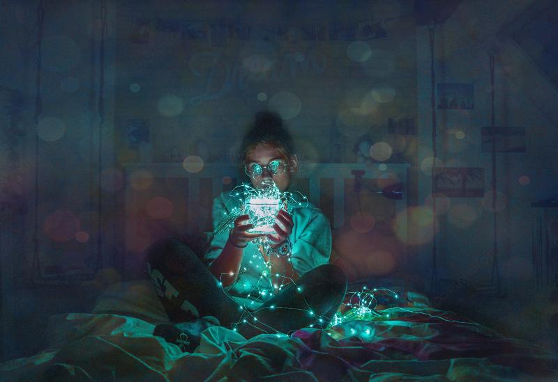 man holding blue string lights in a bowl while sitting in bed