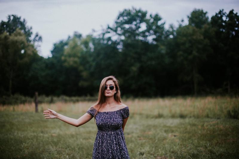 woman stands in field with hand letting go of something