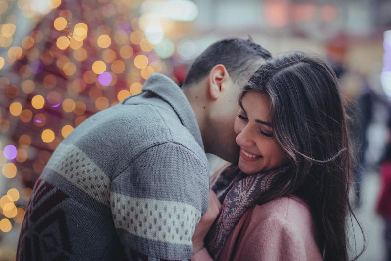 man kisses woman on the cheek by Christmas lights