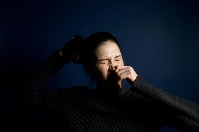 woman sneezes with her eyes closed and holding her hair