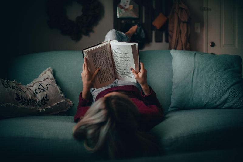 woman lays upside down on couch while reading a book