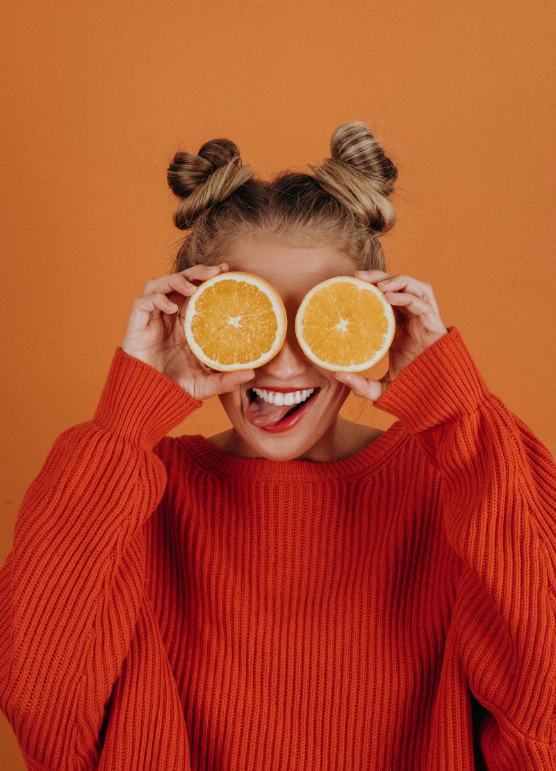 woman holding orange slices to her face in front of orange background