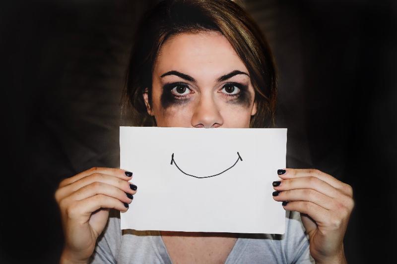 woman holds up smiley face drawing to her face