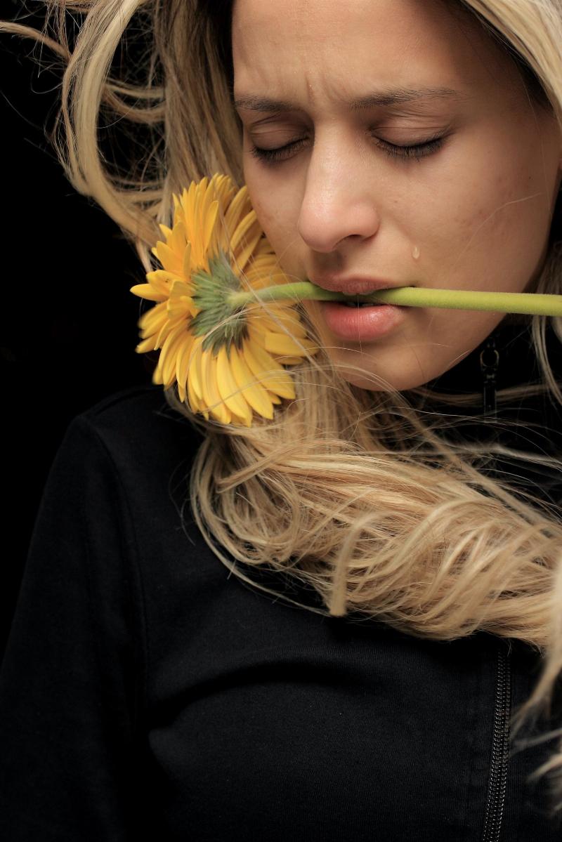 woman holding yellow flower in her mouth looking sad