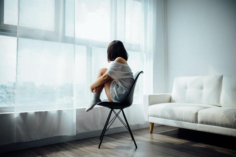 woman holding her knees in while sitting in a chair by the window