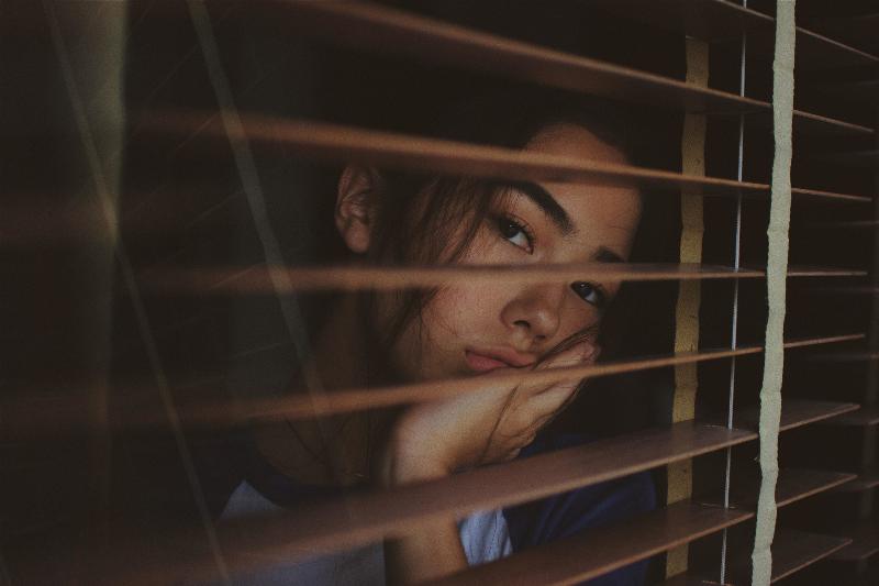 woman looking out window blinds