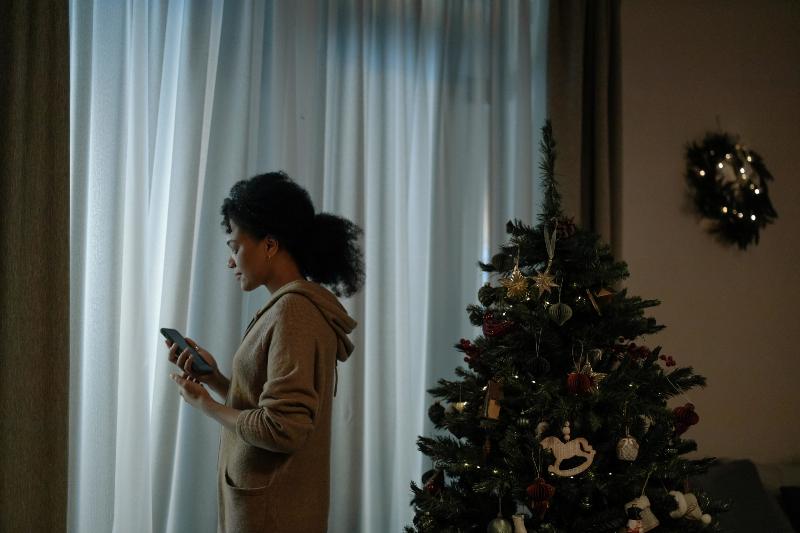 woman checking her phone by christmas tree