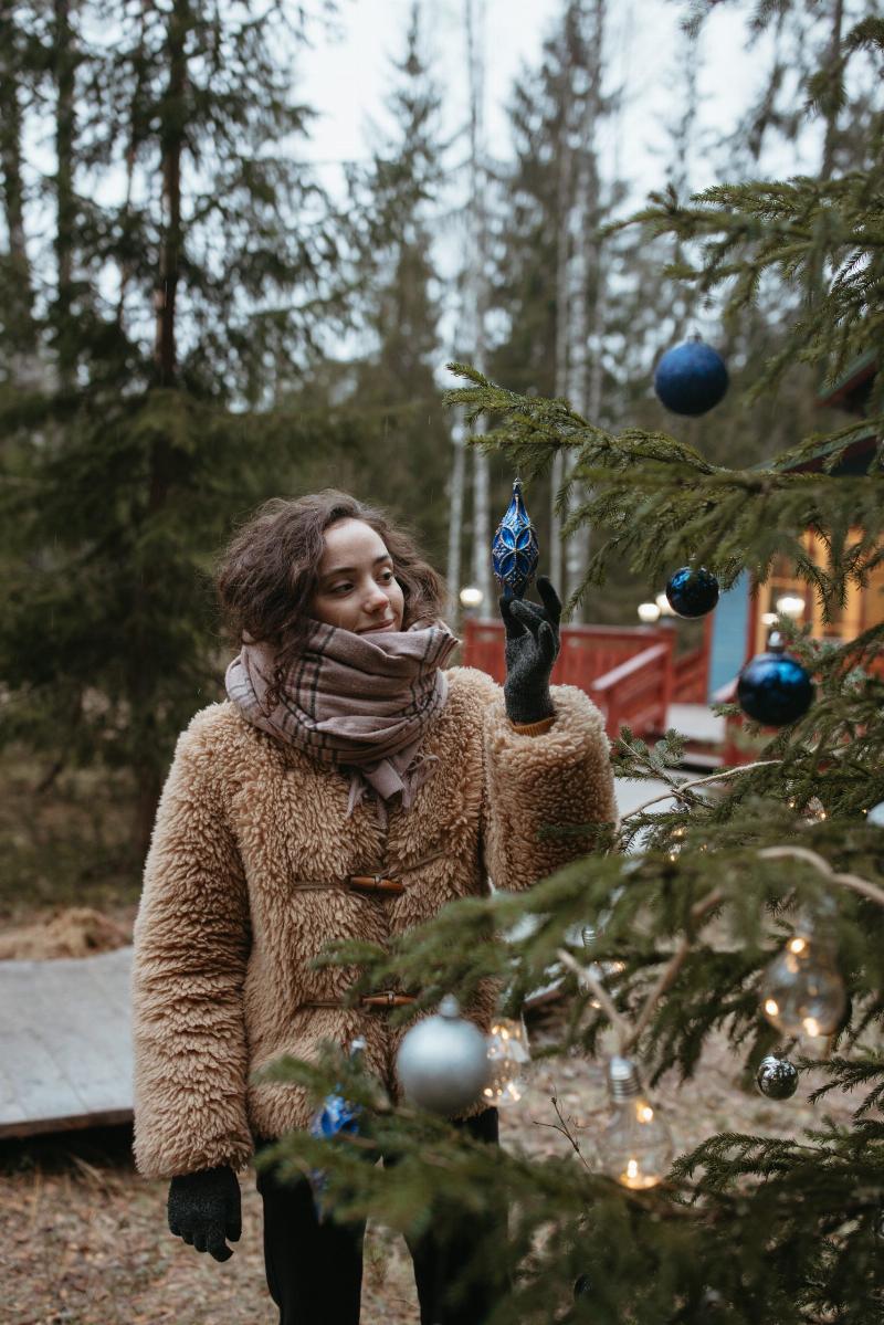 woman hanging Christmas ornaments on tree outdoors