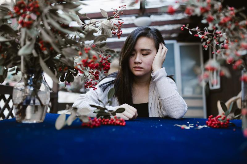 woman looks rests her hand on her face and looks sad while sitting outside by Christmas decor