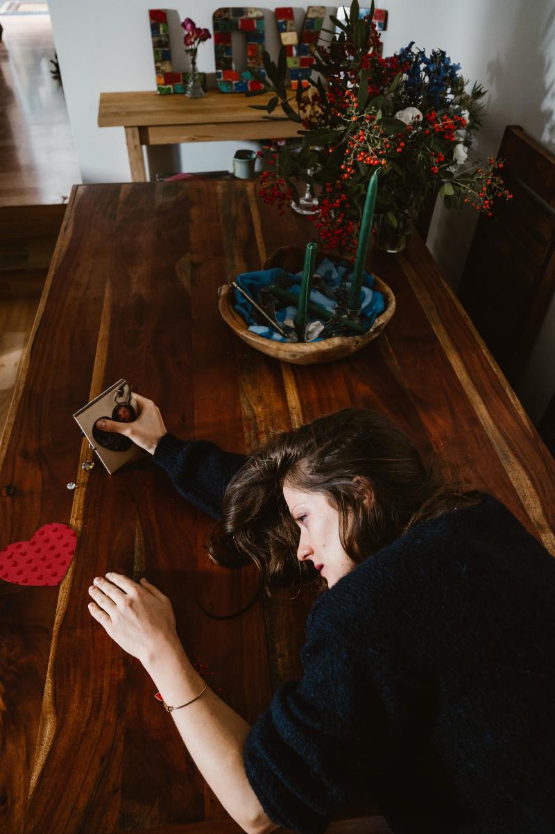 woman sits at wooden table and lays her head on it crying while holding a heart shaped photo frame