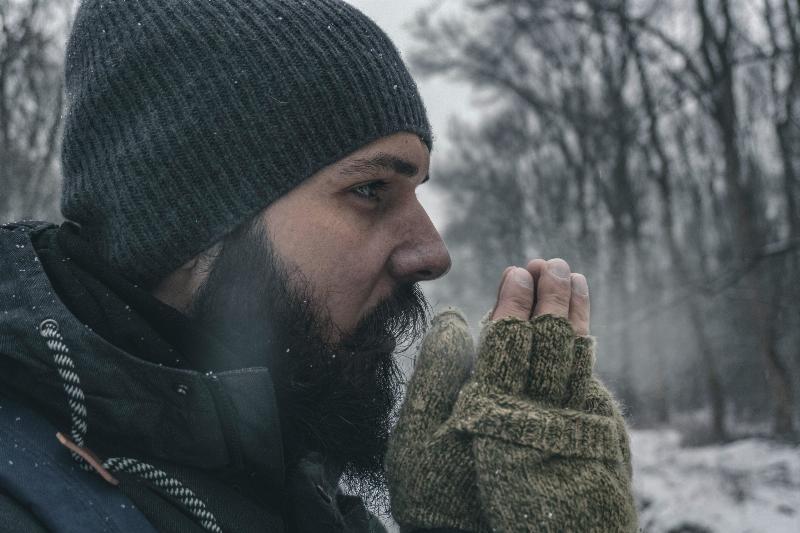 man in snowy forest holding hands close to his face