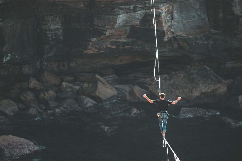 man walking on rope and balancing between cliffs
