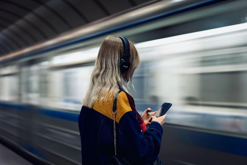 woman listening to music through headphones in front of moving train