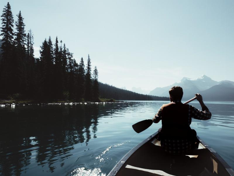 man taking canoe down the water by the mountains