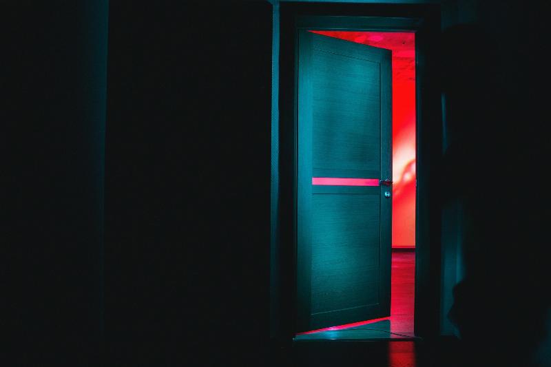 half open door in a dark room opening towards a red room