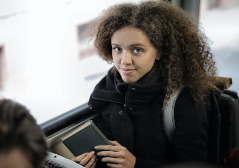 young girl with curly hair holds book on the bus