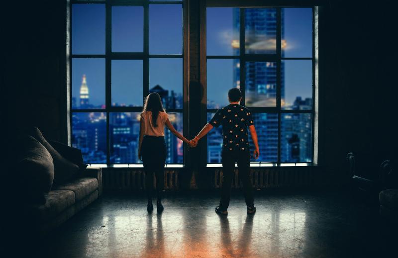 man and woman stand in front of night sky window holding hands