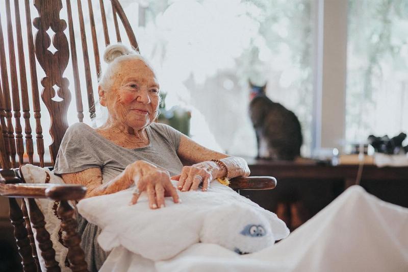 Norma smiles as she sits comfortably in wooden arm chair