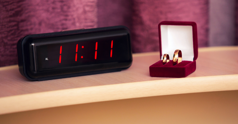 gold wedding rings sitting beside 11:11 showing on the clock