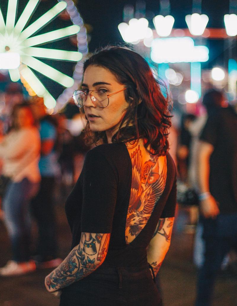 woman looks back while standing at carnival with back covered in tattoos