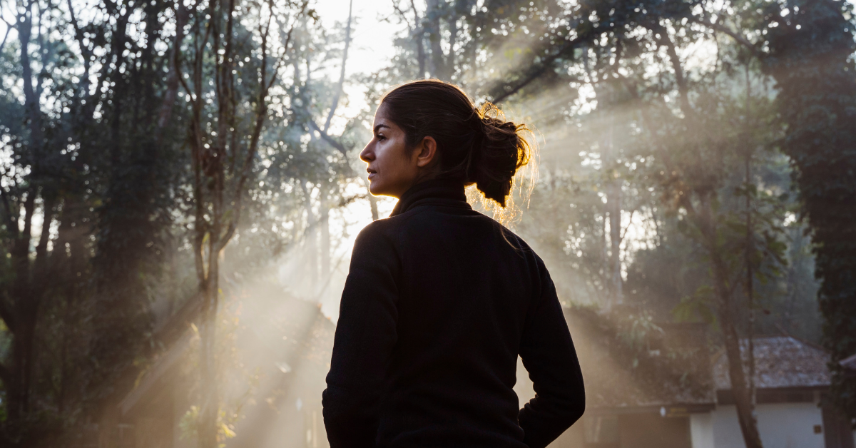woman stands in the sunlight coming through the trees