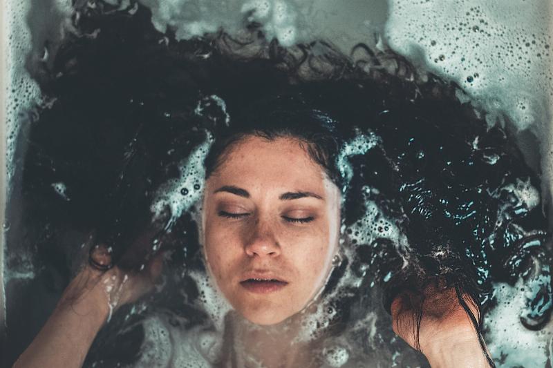woman with eyes closed laying in bubbly bathrub