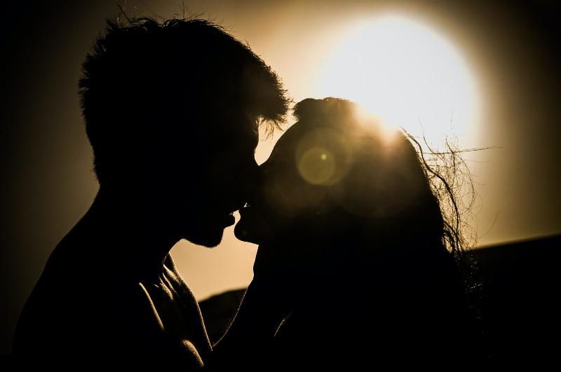 silhouette of man and woman about to kiss by the sun
