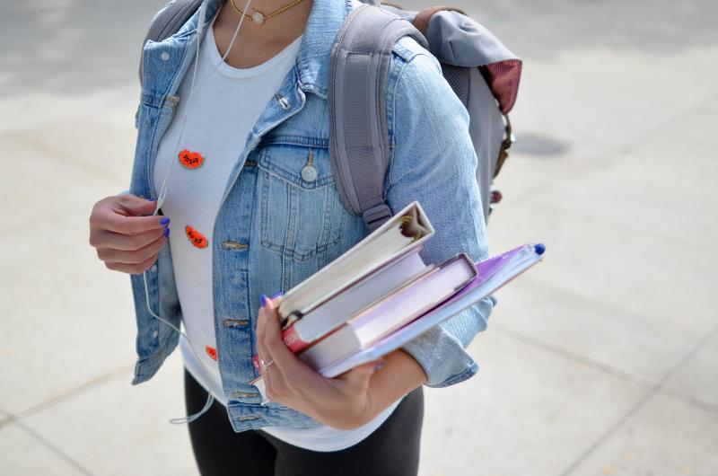 student holding books ad carrying backpack
