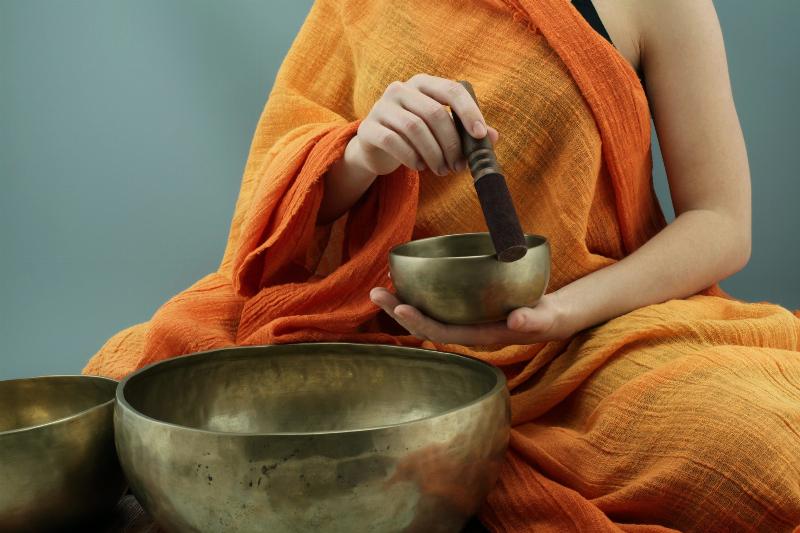 person in orange drap holding spiritual bowls