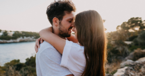 man and woman stand forehead to forehead in an embrace by the sun